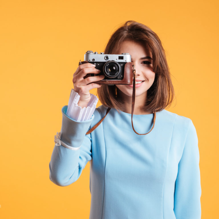 Cheerful woman standing and taking photos with old vintage camer