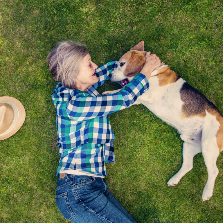 Beautiful senior woman with her dog lying on grass